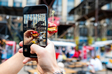 A hand captures a photo of a floating burger against an urban street backdrop