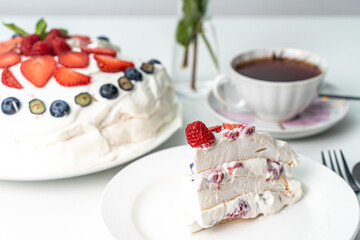 Pavlov cake with strawberries, blueberries and raspberries on whipped cream and a cup of tea on a white table. Selected focus.