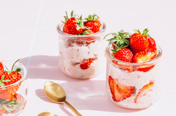 A delightful and healthy breakfast of overnight oats with yogurt and fresh strawberries, beautifully presented in glass jars on a vibrant pink tile table. Bathed in natural sunlight