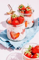 A delightful and healthy breakfast of overnight oats with yogurt and fresh strawberries, beautifully presented in glass jars on a vibrant pink tile table. Bathed in natural sunlight