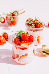 A delightful and healthy breakfast of overnight oats with yogurt and fresh strawberries, beautifully presented in glass jars on a vibrant pink tile table. Bathed in natural sunlight