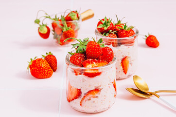 Healthy breakfast of overnight oats with yogurt and fresh strawberries, served in glass jars on a vibrant pink tile table. Bathed in natural light. Selective focus