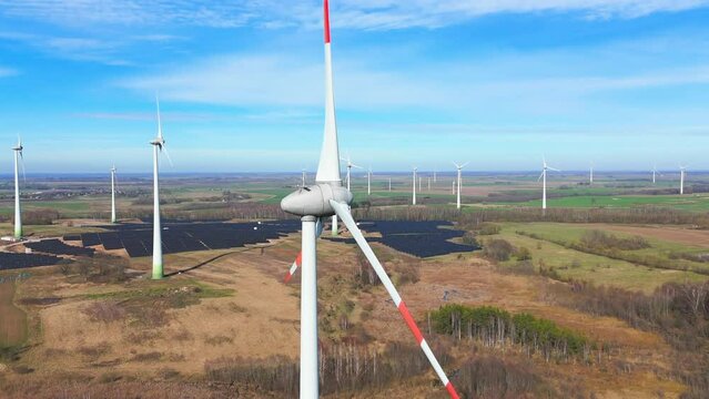 Drone shot of large power plant of solar panels in Electrum solar park and wind turbines in a vast field on a sunny day in Taurage, Lithuania