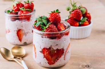 A wholesome and nourishing breakfast of overnight oats with yogurt and fresh strawberries, served in glass jars on a rustic wooden table. Soft, diffused light creates a warm and inviting atmosphere