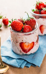 A wholesome and nourishing breakfast of overnight oats with yogurt and fresh strawberries, served in glass jars on a rustic wooden table. Soft, diffused light creates a warm and inviting atmosphere