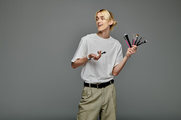 Handsome man holds multiple brushes for makeup.