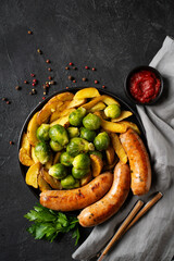 Bavarian sausage and brussels sprouts, potatoes on black plate or pan, parsley, tomato sauce