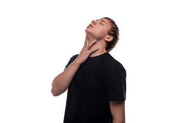 Cute teenage guy with blond hair dressed in a black T-shirt holding his neck