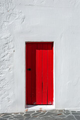 A vibrant red door stands alone in the center of a white wall, casting a slight shadow. The design is simple and clean, highlighting the door as the focal point.