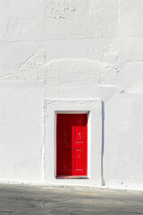 A vibrant red door stands alone in the center of a white wall, casting a slight shadow. The design is simple and clean, highlighting the door as the focal point.