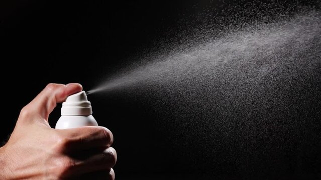 Slow motion of spray bottle drops on black background. Male perfume bottle on a dark background