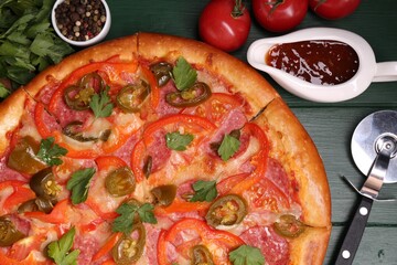 Delicious pizza Diablo, ingredients and cutter on green wooden table, flat lay