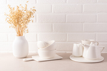 A set of white ceramic tableware for a tea ceremony, a vase with ears of wheat on a stylish countertop. a white brick wall. Cozy bright kitchen.