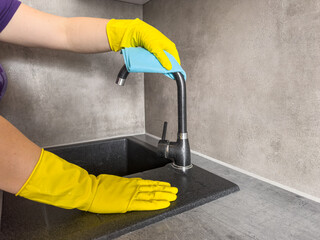 woman in yellow gloves and sponge cleaning and disinfects kitchen sink