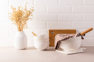 Set of White Stylish Ceramic Bowls for Cooking, White Gypsum Vase with Ears of Wheat on Kitchen Countertop. White brick wall. Eco-friendly kitchen.