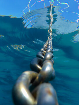 Ancor chain and reflected boat in turquoise crystal clear seawater.