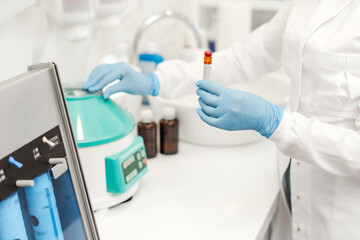 Laboratory technician, nurse or doctor holding test tube, standing in equipped medical laboratory