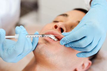 Beautician doctor holding injection, lip plumping to handsome young man, patient, cosmetic procedure