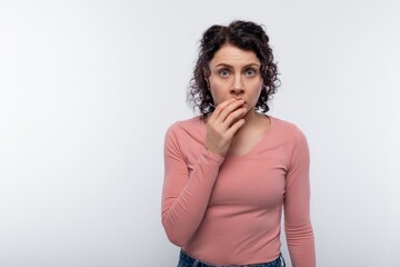 Brunette with curly hair in a pink blouse is surprised and covers her mouth with her hand