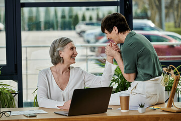 Two women work together at a laptop in an office setting.