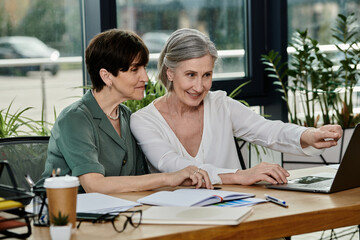 Two women collaborate on a project while reviewing information on a laptop.