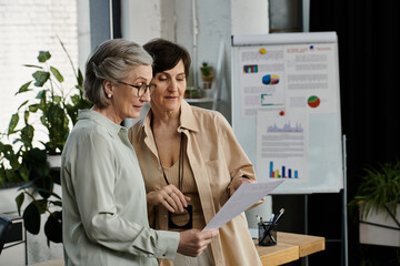 Two women pose by graphs and working together.
