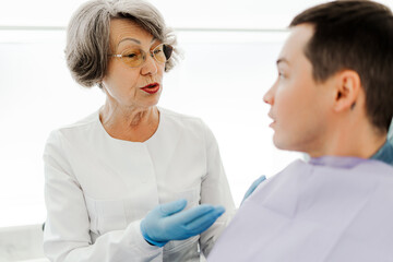 Obraz premium Mature, senior woman, dentist doctor talking to young attractive patient, she explaining something