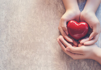 Adult and child hands holding a red heart on an aqua background symbolize heart health, donation, corporate social responsibility, World Heart Day, World Health Day, and Family Day.