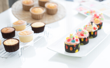 Selective focus on cupcakes with decorations on plate. Fresh baked cupcakes on rack for decorating in paper cups on white table