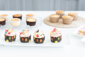 Selective focus on cupcakes with decorations on plate. Fresh baked cupcakes on rack for decorating in paper cups with Icing candy and jelly on white table