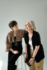 Middle-aged lesbian couple sitting closely together on a stool in a photo studio.