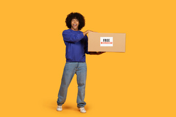 A man is standing and holding a box, which has a free delivery sign on it. He seems to be ready to deliver the package to a customer.
