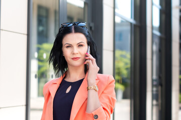 Successful businesswoman or female CEO on the phone or chat on the internet with business partner while walking along the street of the company building. Urban lifestyle concept.   