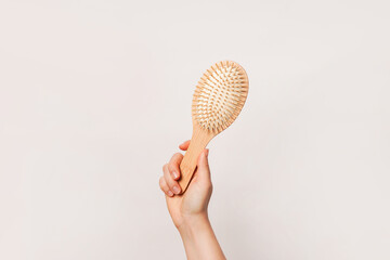A hand is holding a wooden hairbrush against a plain background