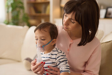 Mother holding baby boy in her arms and giving him an inhalation