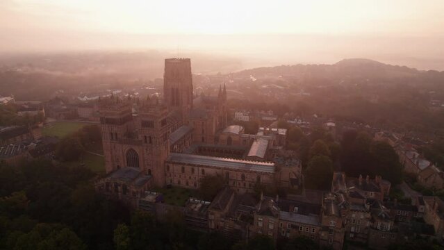 Drone tracks around the facade of Durham Cathedral on a beautiful, misty summer dawn. Low fog is seen in the town 