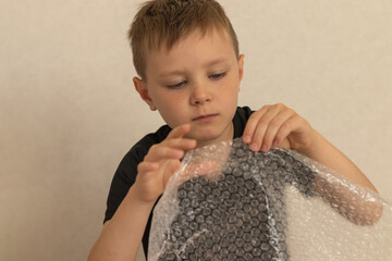Boy popping bubble wrap indoors. Close-up image