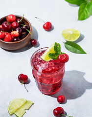Cherry-lime mojito cocktail with mint, lime and ice on a light background with fresh berries and shadow.