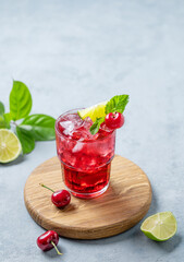Cherry-lime mojito cocktail with mint, lime and ice on a wooden board on a blue background.