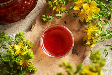 Red oil made of St. John's wort flowers in a bowl with fresh Hypericum plant