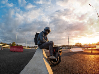 A rider wearing a helmet on an electric monowheel . Modern urban transport . At sunset
