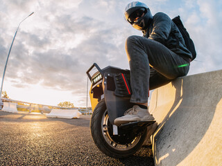 A rider wearing a helmet on an electric monowheel . Modern urban transport . At sunset © pavelkant