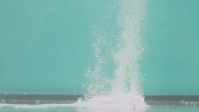 A one white round effervescent pill on a turquoise background falls into the water. Two tablets lie at the bottom of the container, dissolve, fizz to form bubbles and powder. The concept of testing