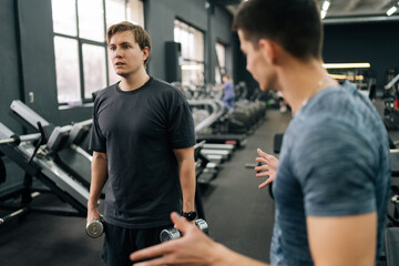 Motivated beginner sportsman working out with dumbbell with personal fitness trainer at gym. Sporty guy doing weight exercises with assistance of coach. Concept of healthy lifestyle, physical activity