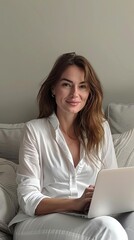 front photo of attractive 35 yr old polish woman wearing a white shirt sitting on a couch and working on a laptop