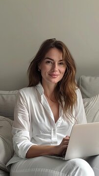 front photo of attractive 35 yr old polish woman wearing a white shirt sitting on a couch and working on a laptop