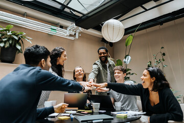 Happy male and female entrepreneurs stacking hands in business meeting at office