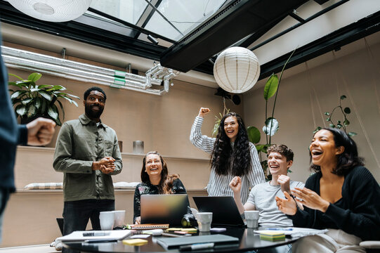 Multiracial male and female entrepreneurs cheering during team meeting at office