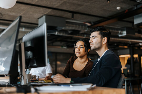 Young male and female computer programmers sharing computer sitting at desk in office