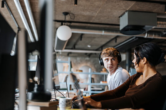 Male entrepreneur with headphones talking to female colleague sitting at office